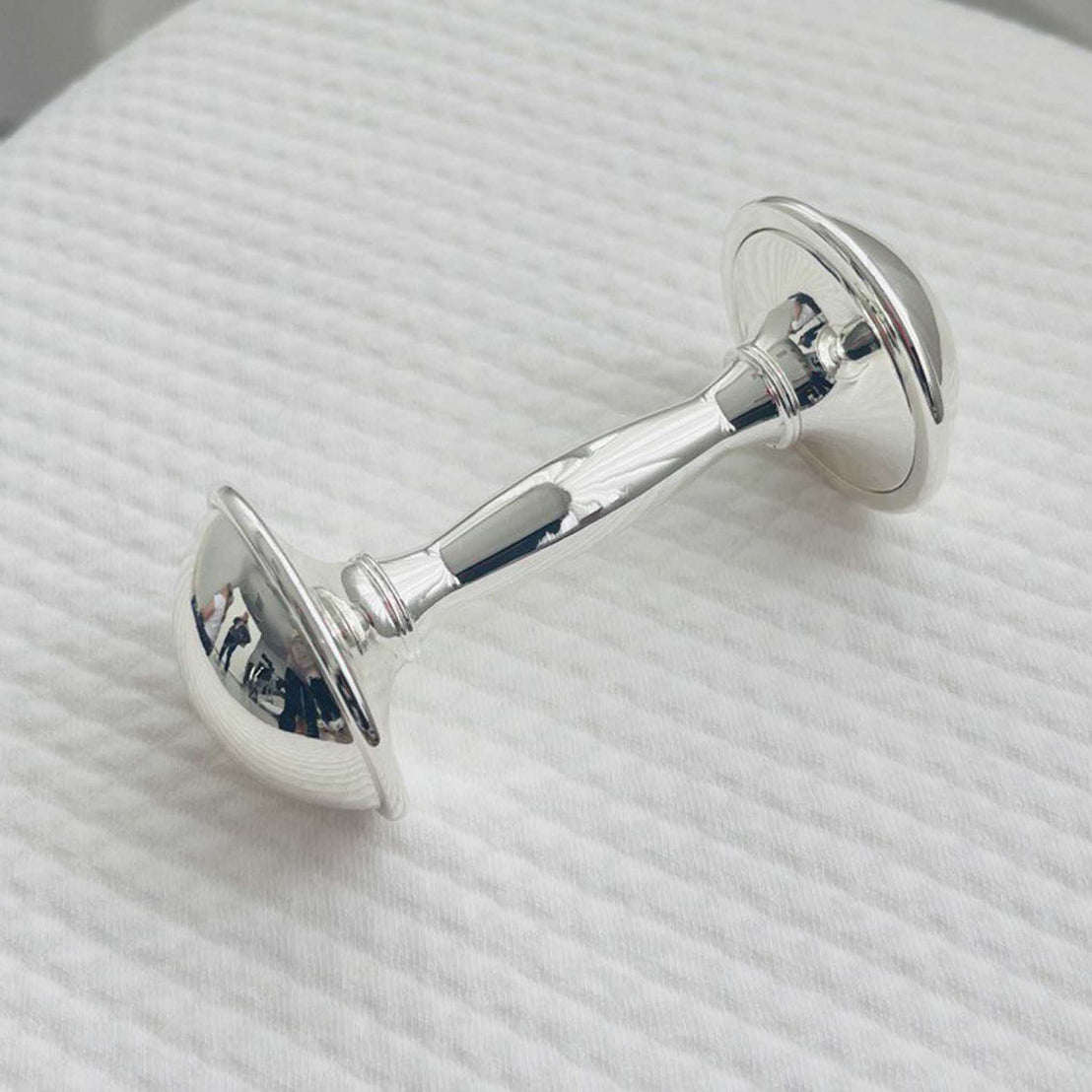 Silver plated dumbbell baby rattle on a white textured surface
