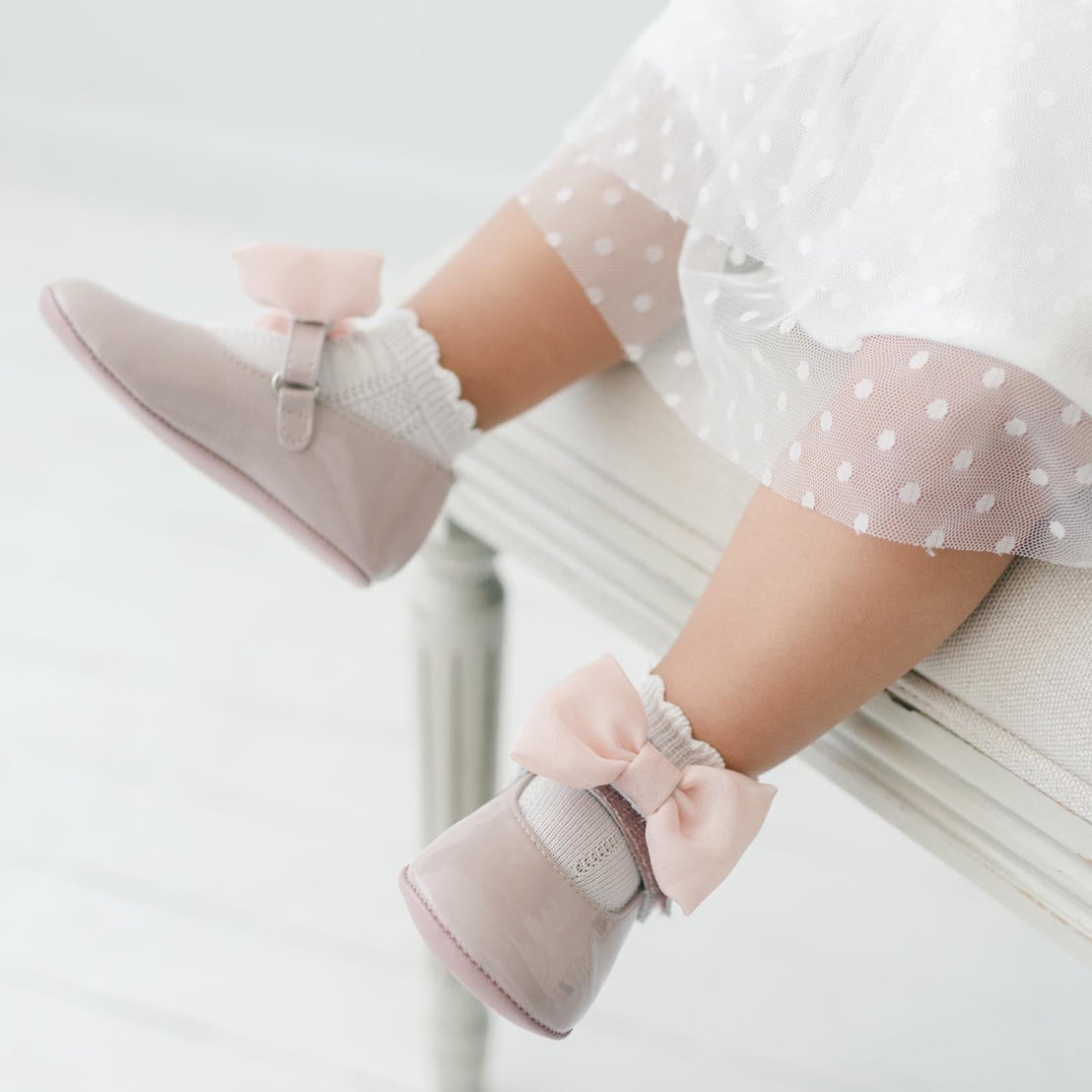 Baby's legs wearing pink Mary Jane shoes  with bows.