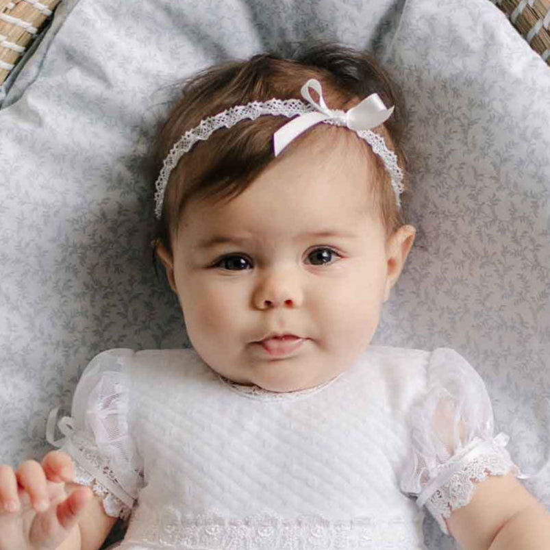 Baby wearing the Stella Silk Ribbon Headband and matching Dress against a patterned blanket. 