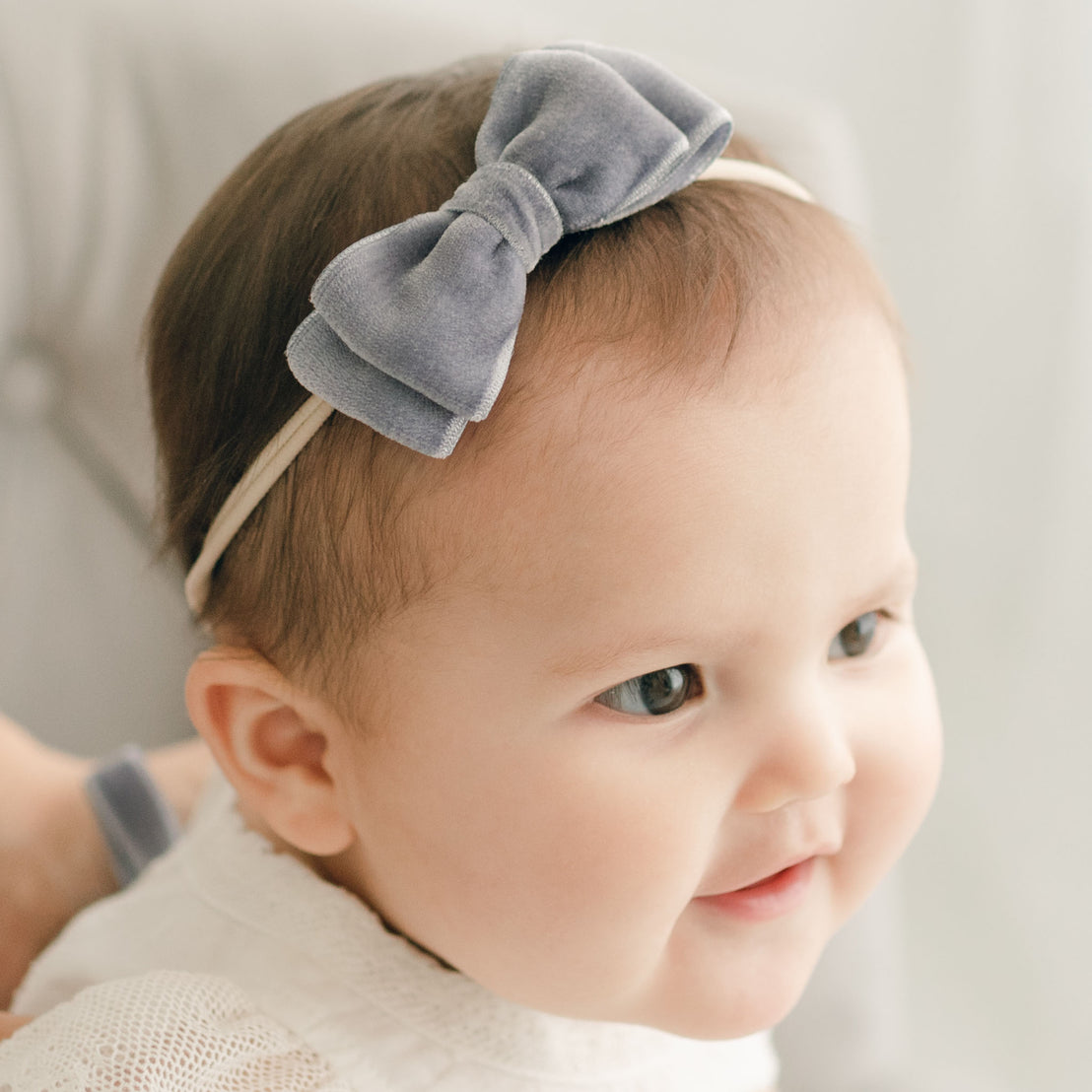 Baby girl wearing the heather Emily Velvet Bow Headband with hand-stretched nylon band.