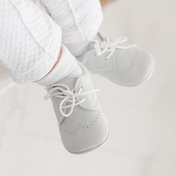 Photo of a baby wearing the Dove Grey Suede Shoes crafted with a super soft, dove grey suede with detailed edging.