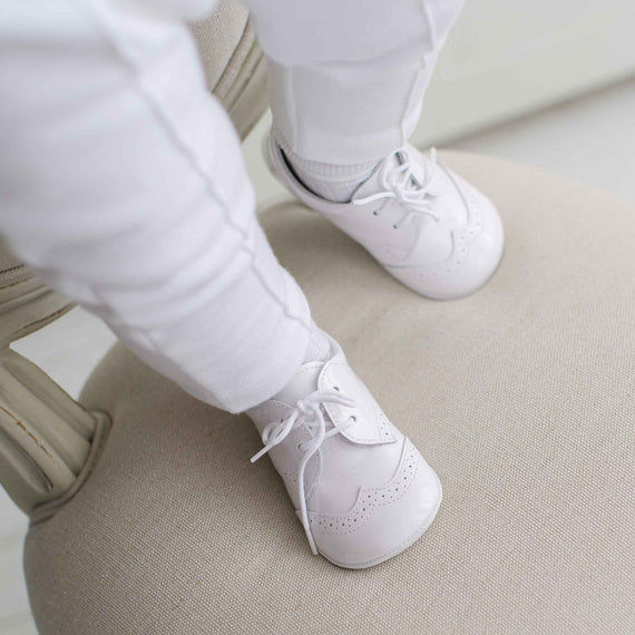 White baby shoes worn with white pants on a light-colored floor.