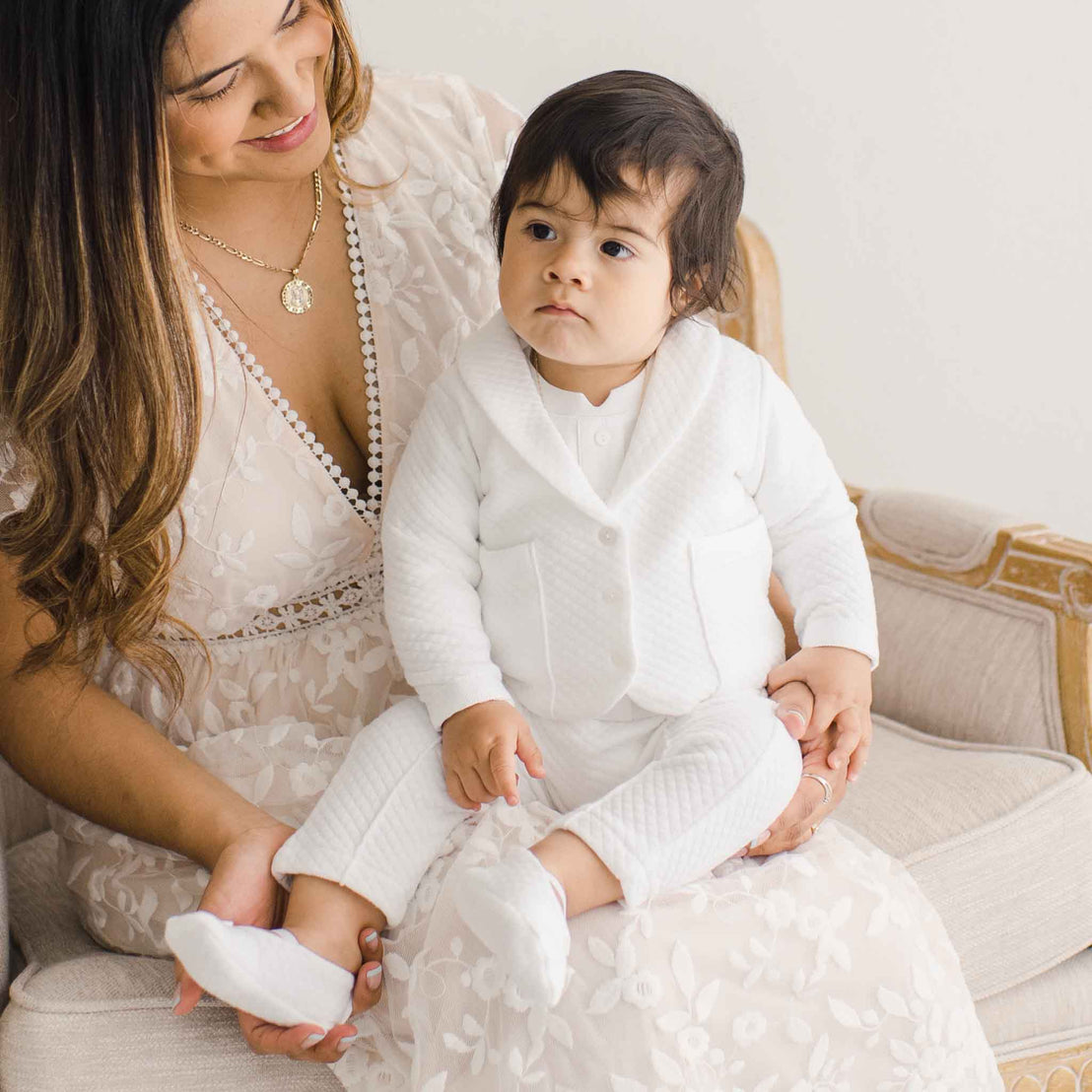 Baby boy sitting on his mother's lap and wearing the Elijah 3-Piece Suit made from 100% white textured cotton jacket and pants, and a white cotton / rayon blend shirt