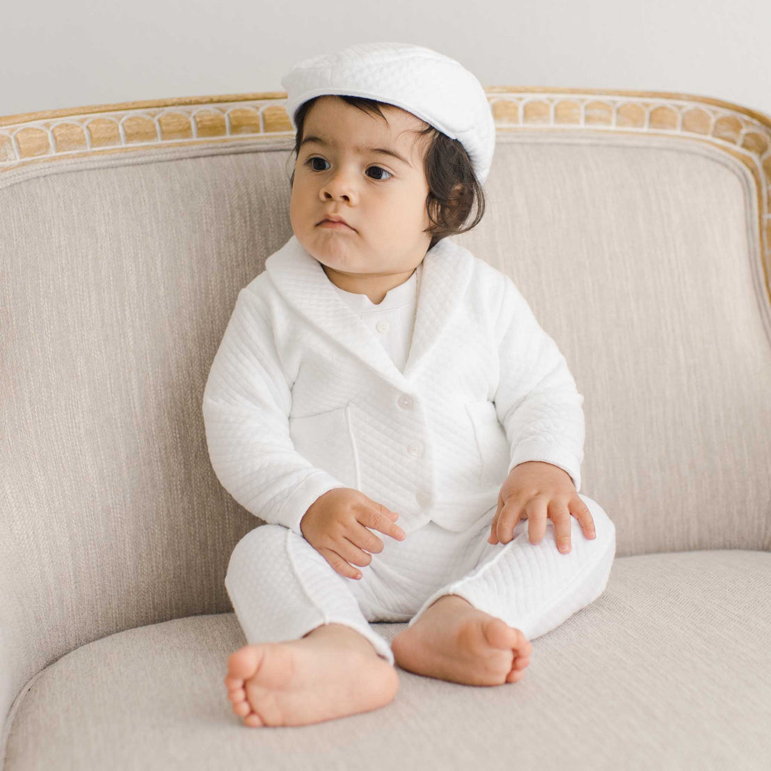 Baby boy sitting on a chair wearing the Elijah 3-Piece Suit made from 100% white textured cotton jacket and pants, and a white cotton / rayon blend shirt