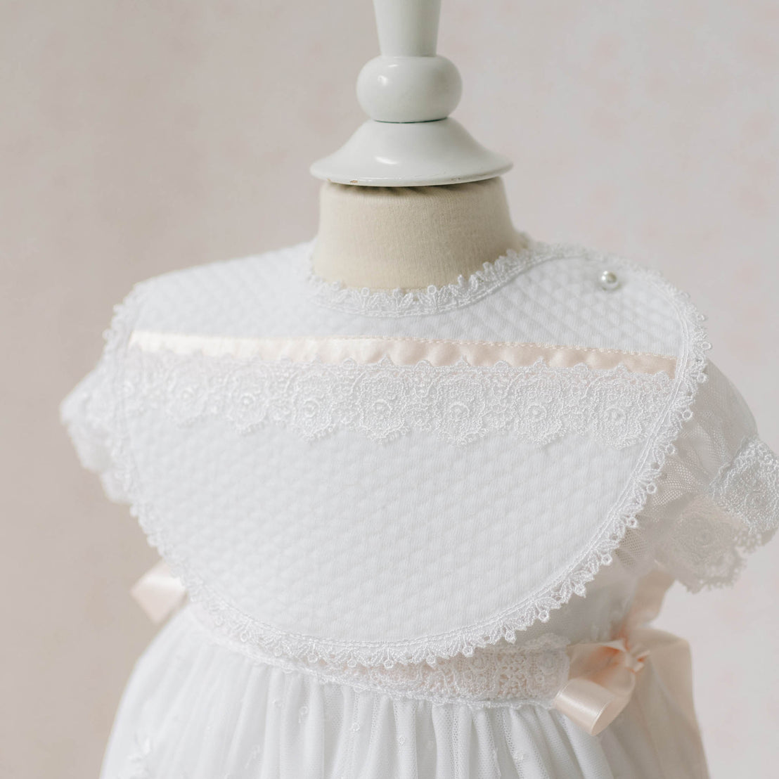 Close up photo of the Melissa Bib on a mannequin against a plain background. Details show white quilted textured cotton with Venice lace and silk ribbon. Perfect baptism gift ideas.