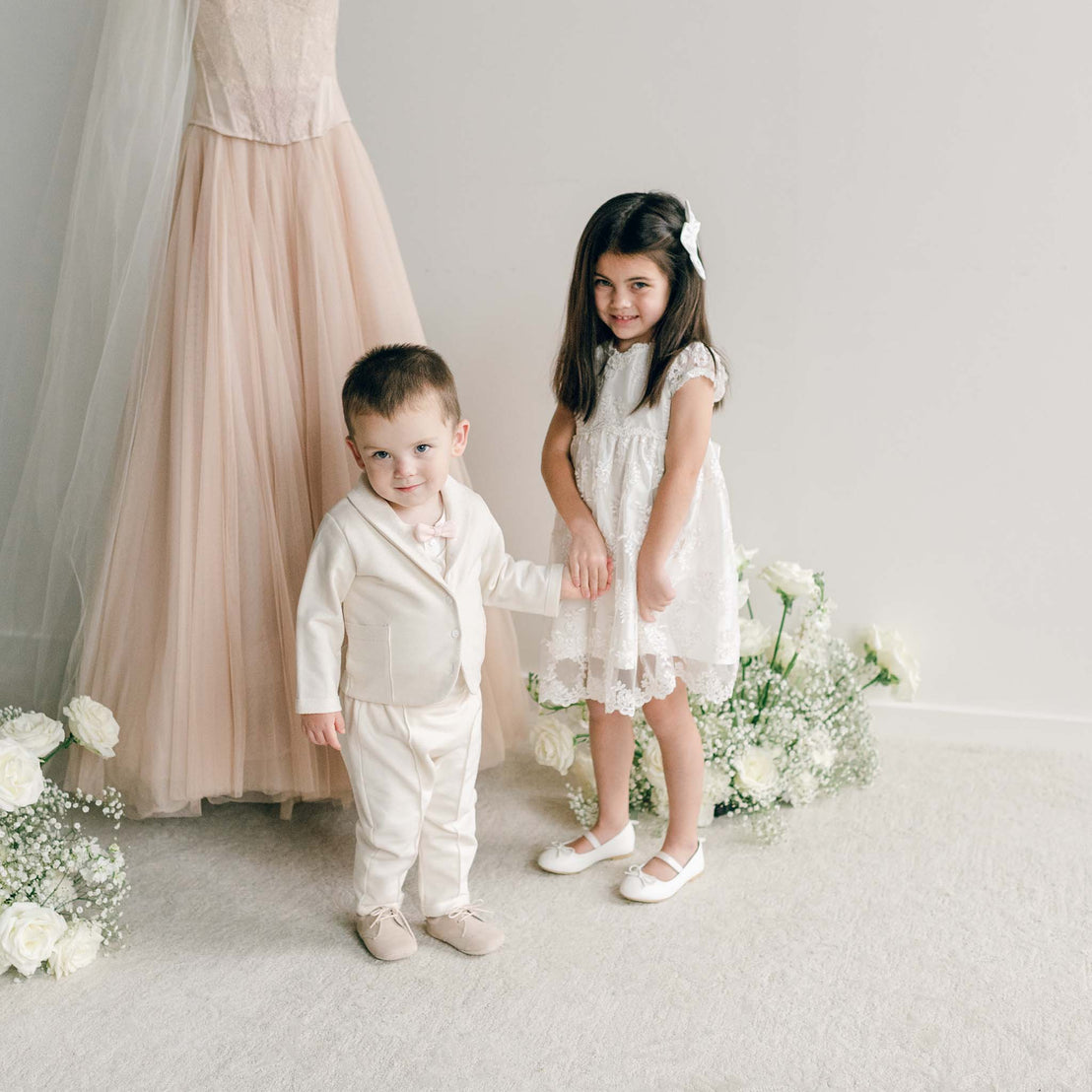 Little girl wearing the Penelope Lace Dress holding hands with a boy dressed in a cream suit.