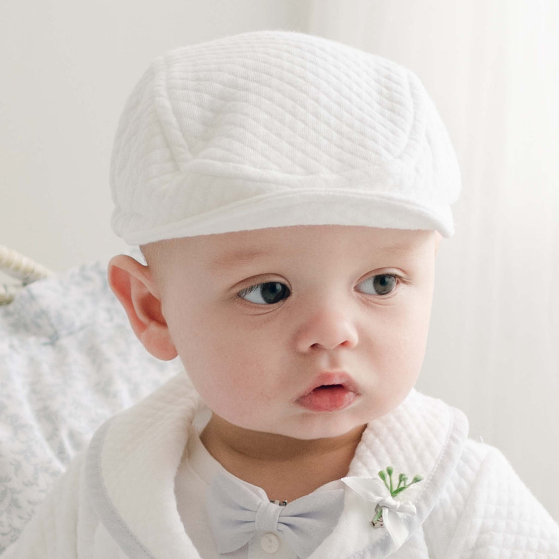Close-up of a baby wearing the Harrison Quilted Newsboy Cap, complemented by a matching quilted suit and a bow tie, against a softly lit background.