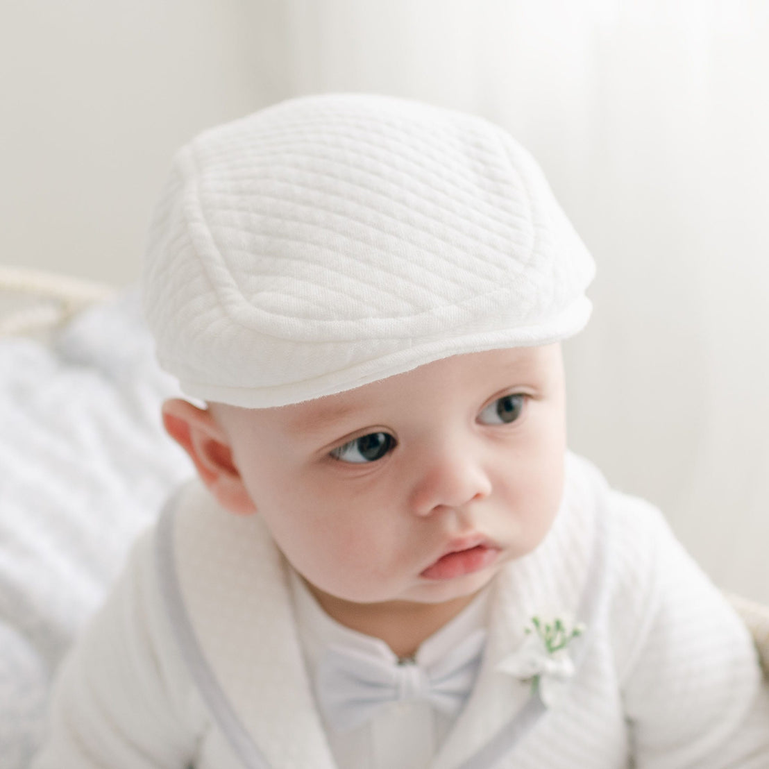 Close-up of a baby wearing the Harrison Quilted Newsboy Cap, showcasing its soft white quilted fabric and tailored design.