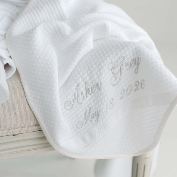 White baby booties with embroidered text on a light wooden surface