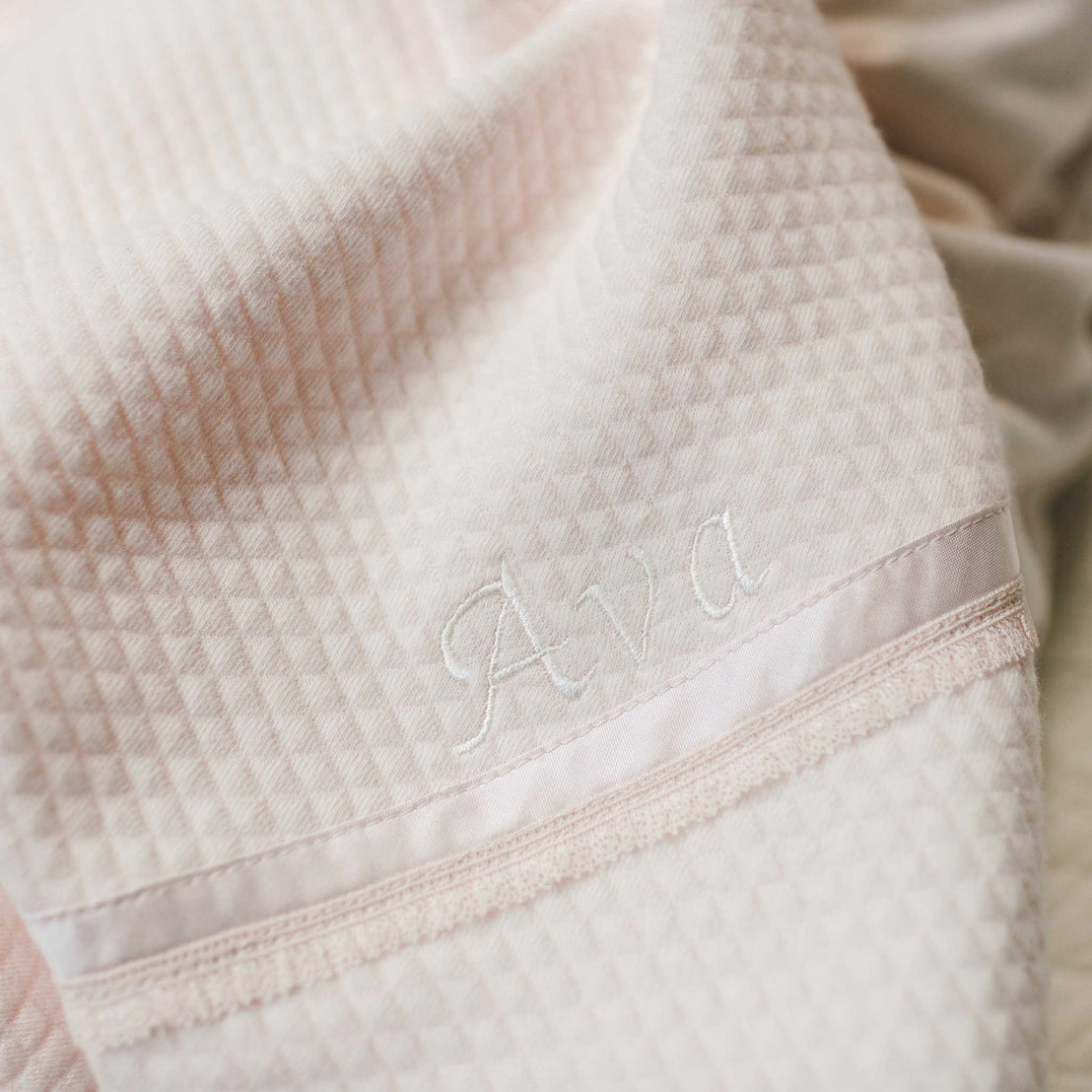 Close-up detail of the custom embroidered name "Ava" on the corner of the Ava Personalized Quilt Blanket. Corner detail also features champagne dupioni silk and pink lace trim. 