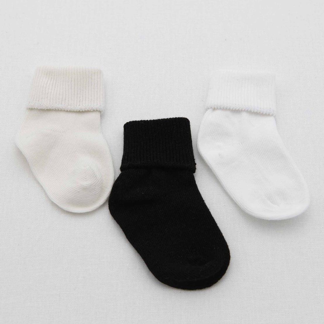 Three Boys Simple Socks, one in ivory, one in black, and another in white, are displayed on a light gray background.
