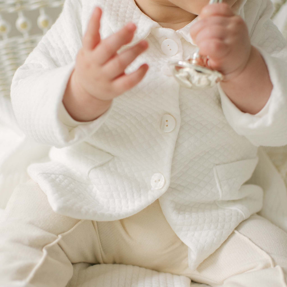 Close-up photo of a baby boy wearing the Braden Coat Suit. Details show the texture of the ivory quilt jacket and buttons.