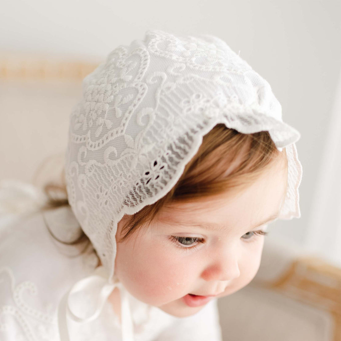 A toddler with light brown hair wearing an Eliza Bonnet and matching dress gazes downward with a gentle expression.