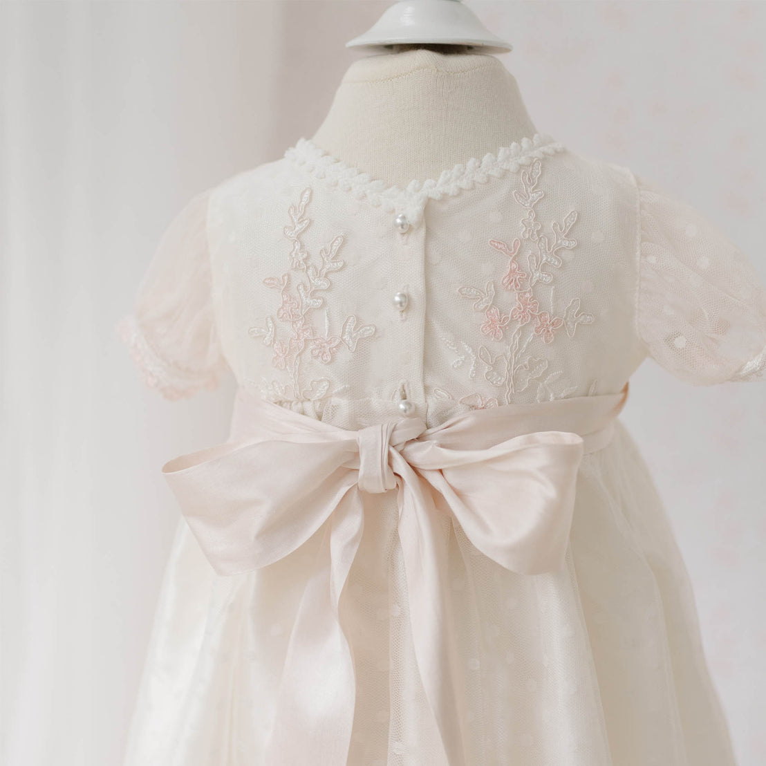 Close-up back view of the Elizabeth Newborn Christening Dress on a mannequin featuring the floral embroidery lace and a silk bow against a white background. Part of the Baby Beau & Belle Baby Girl Christening Dress Collection.