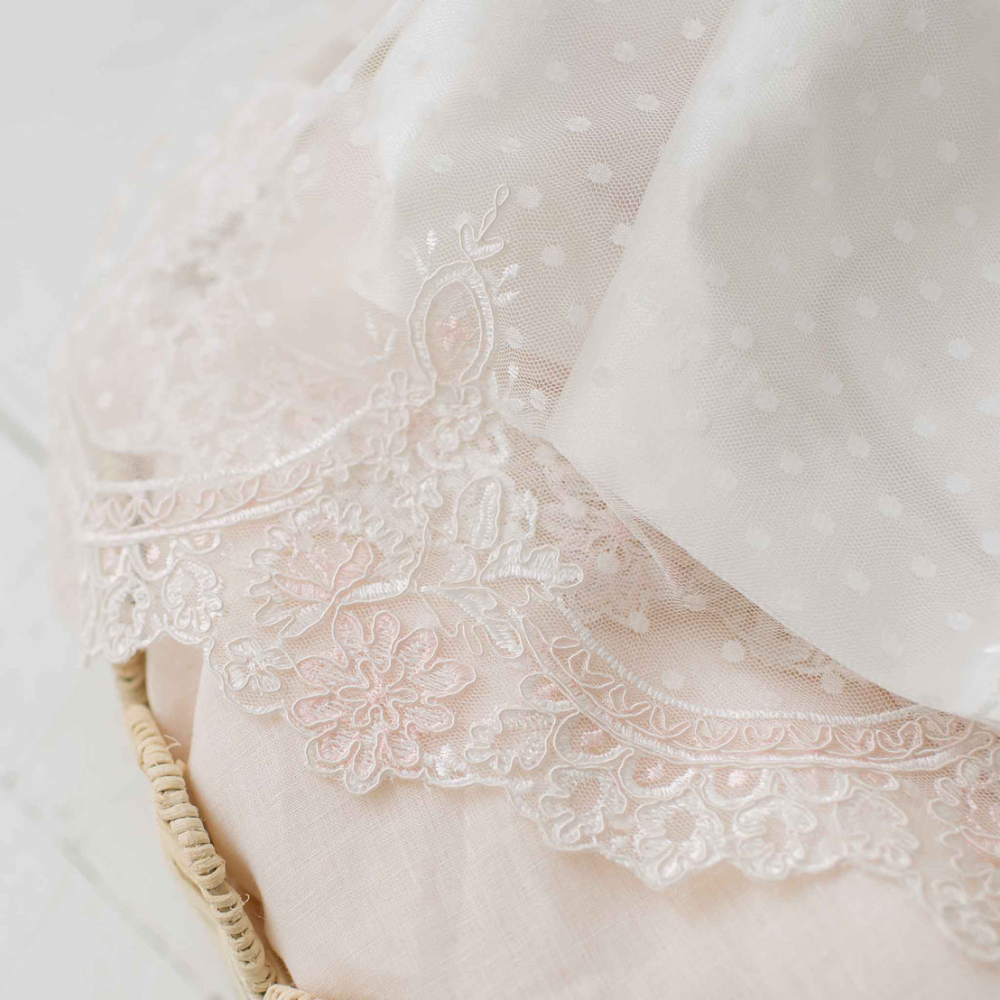Close-up of the scalloped lace at the hem of the skirt on the Elizabeth Newborn Christening Gown showcased atop a pink linen lined crib.