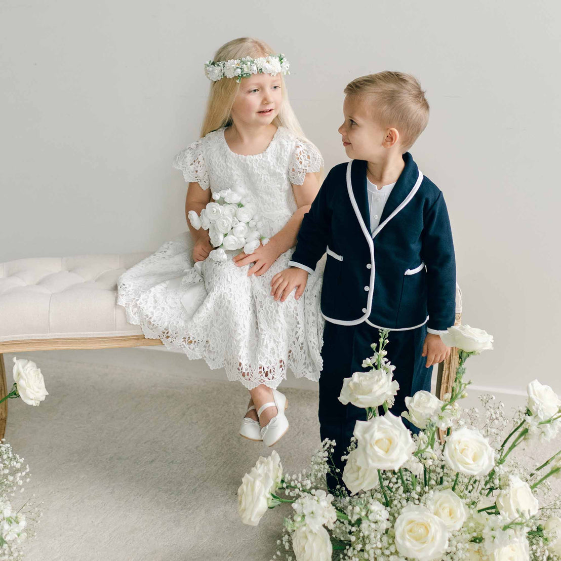 A boy in the Elliott 3-Piece Suit standing next to a girl seated on a bench, surrounded by white roses.