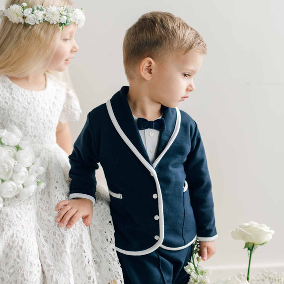 A young boy wearing the Elliott 3-Piece Suit, standing beside a girl dressed in lace while looking off to the side.