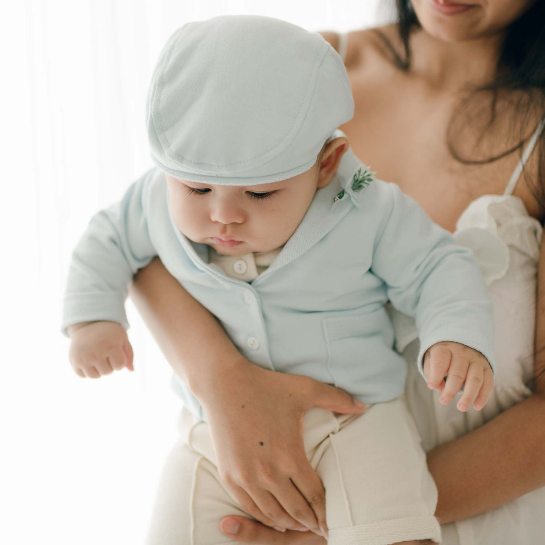 Close-up of a baby wearing the Ezra Powder Blue 4-Piece Suit and matching cap while being held.