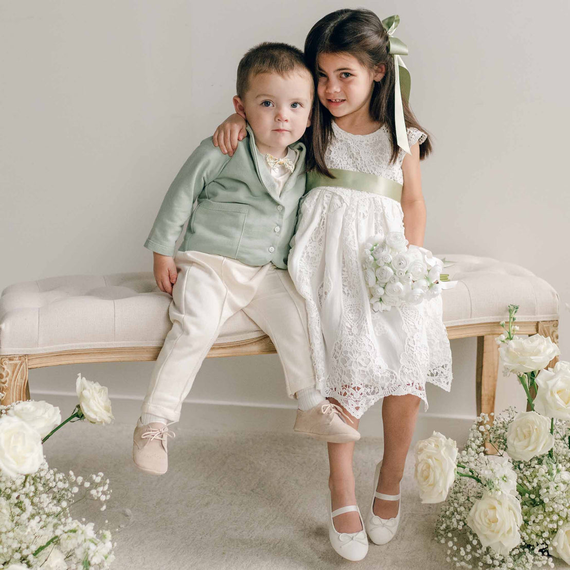 A toddler wearing the Ezra Sage 4-Piece Suit sits beside a girl in a lace dress, with his arm around her shoulders.