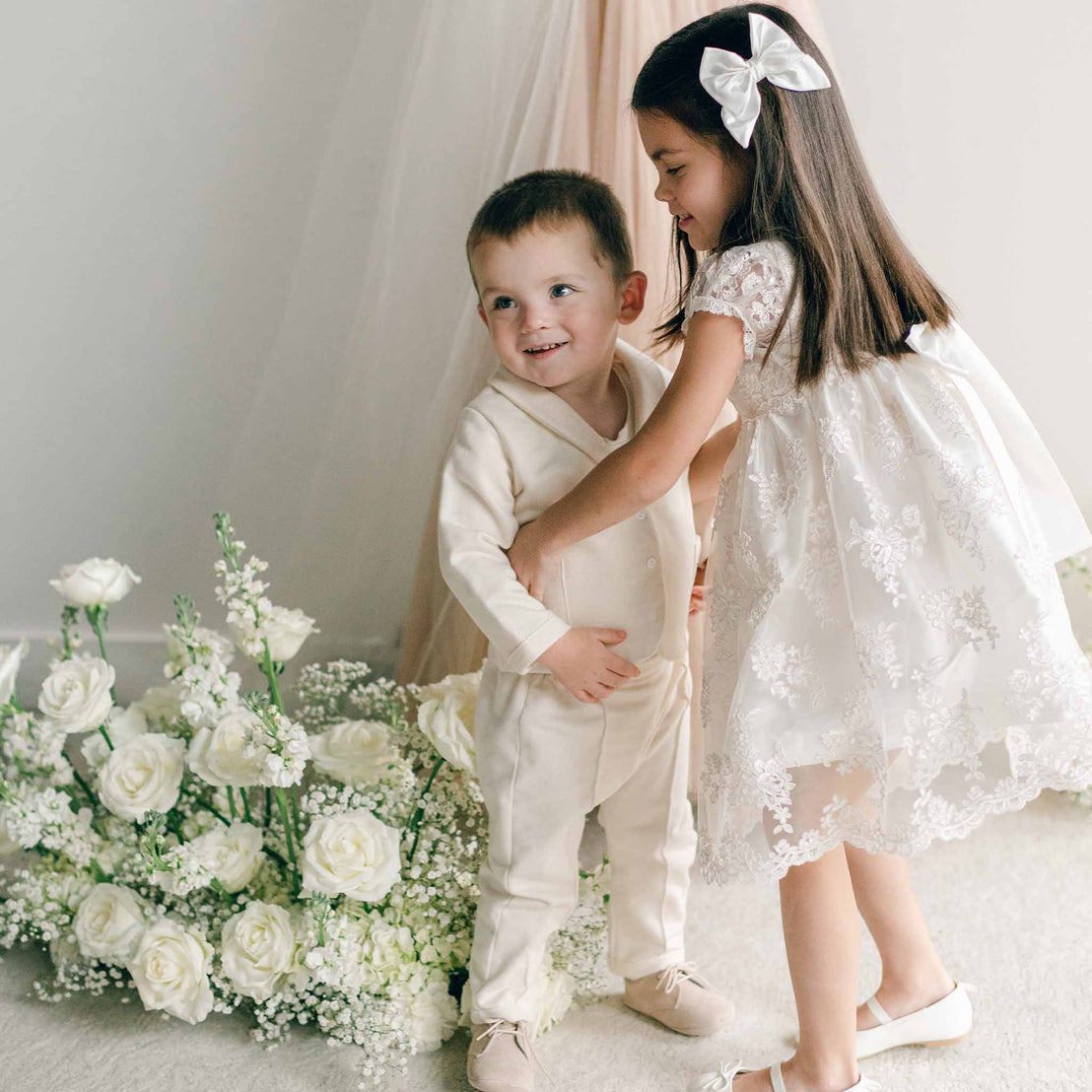 A girl in a lace dress gently hugging a toddler dressed in the Ezra Tan 4-Piece Suit.