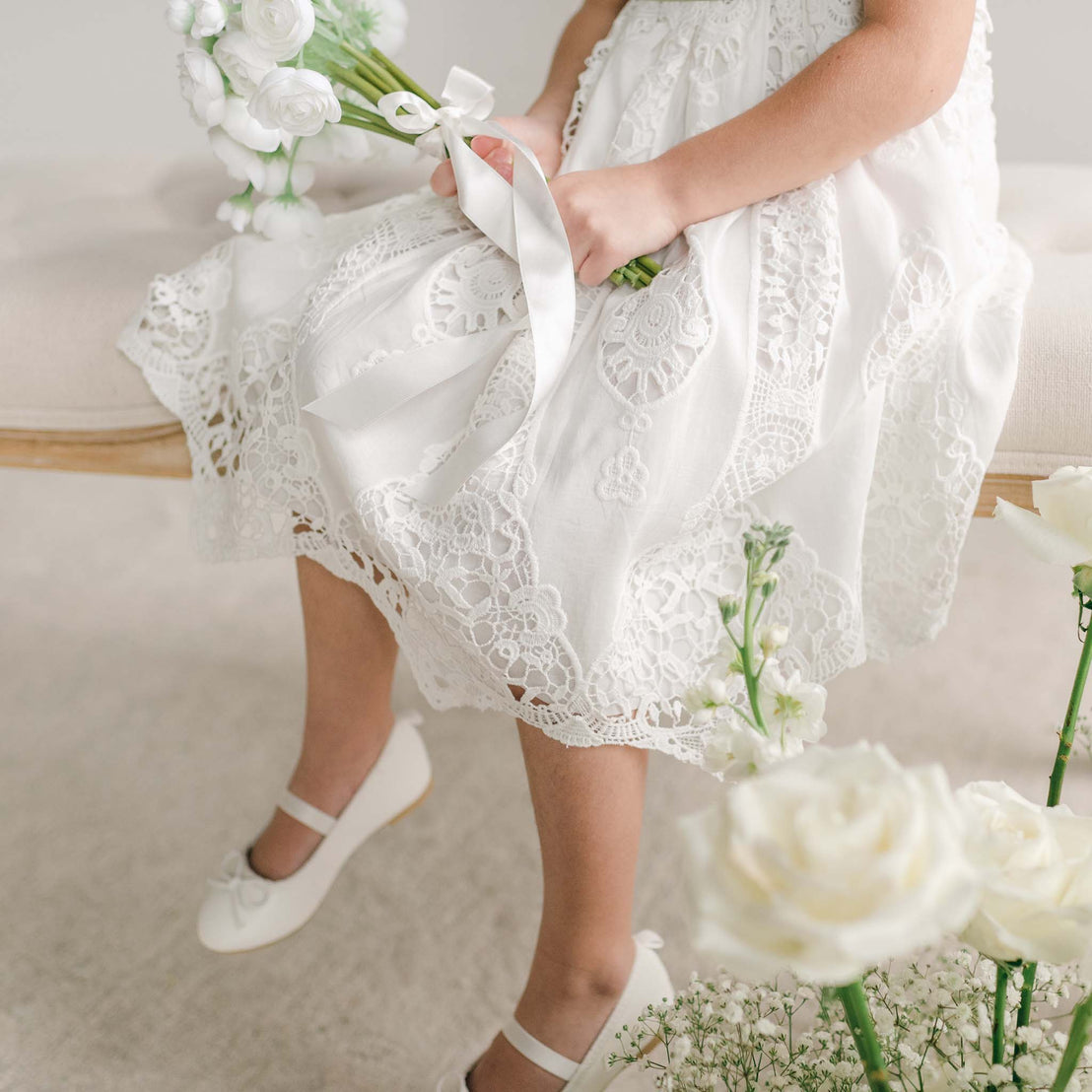 Close-up of a girl holding a white bouquet, showing the detailed lace skirt of the Grace Girls Lace Dress.