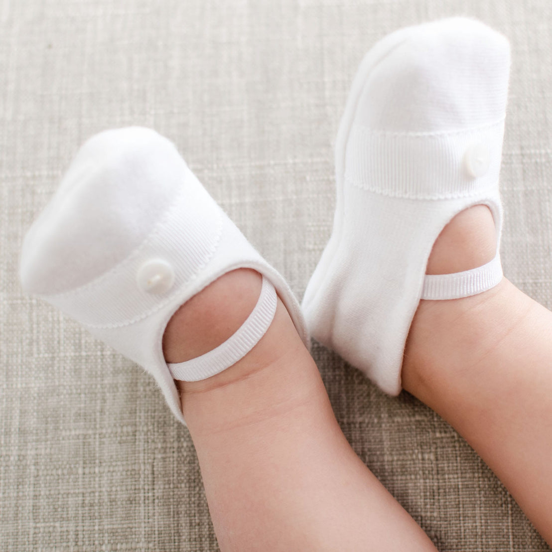 White baby shoes with buttons on a textured surface