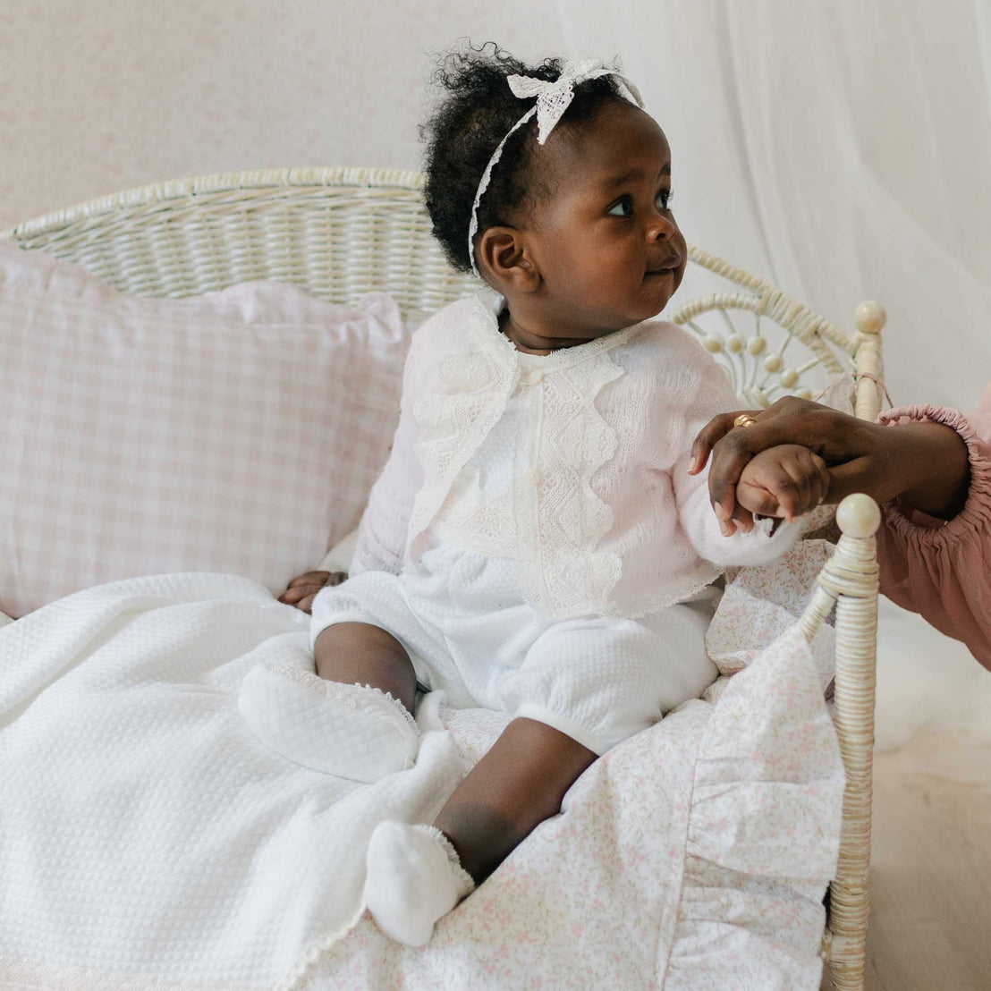 Baby in the Hailey Romper and matching Knit Sweater sits in a white wicker chair with a pink patterned blanket. Part of Baby Beau & Belle's  high end baby clothes.