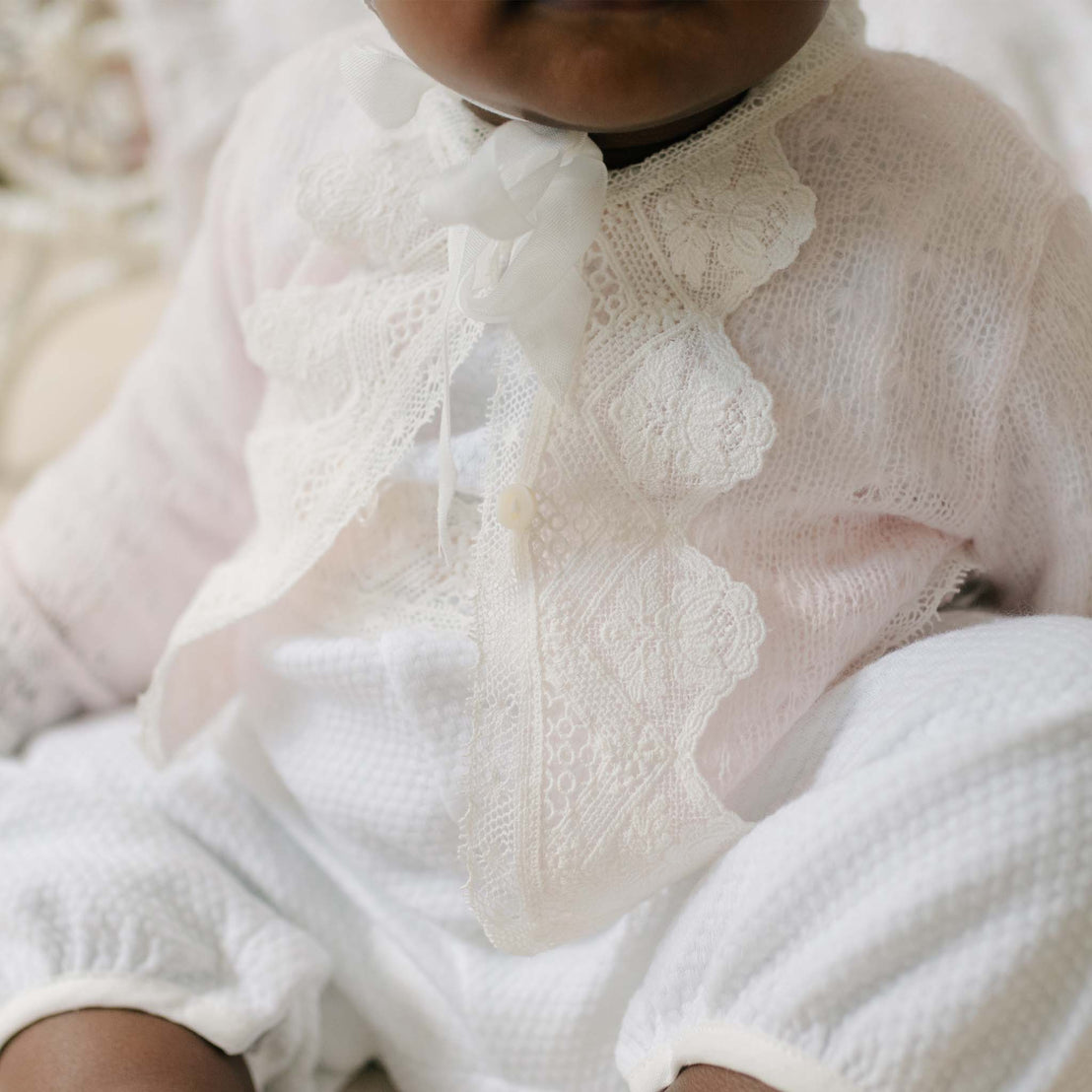 Close up photo of a baby wearing the Hailey Knit Sweater. Details show the delicate soft pink knit and matching light ivory laces. Perfect baptism gifts for girls.