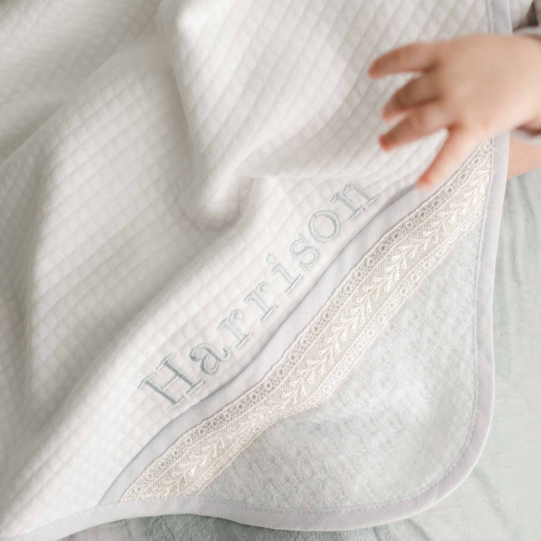 The Harrison quilted blanket with embroidered lace trim and "Harrison" personalization, draped over a surface.