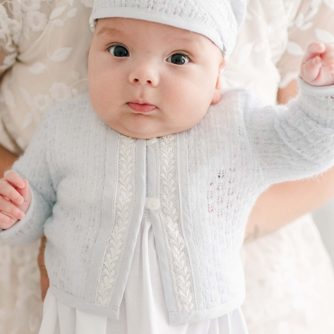 A close-up of the Harrison Newborn Sweater, showcasing the delicate knit fabric, lace trim, and pearl button accents.