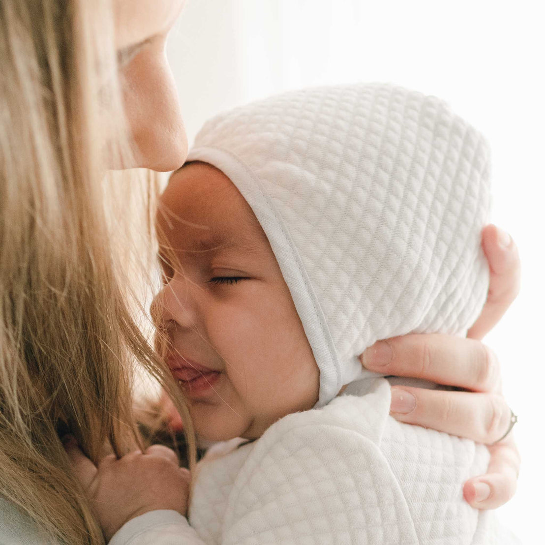 Baby nestled close, wearing the Harrison Quilted Bonnet, emphasizing its comfortable and stylish design.