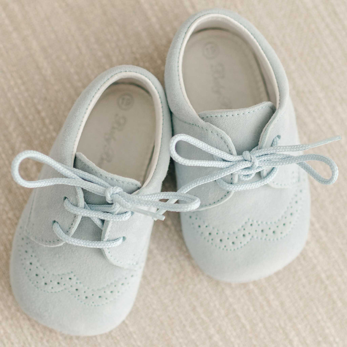 Top view of the Harrison Suede Shoes placed on a textured surface, displaying the gentle blue hue, fine stitching, and secure lace-up closure.