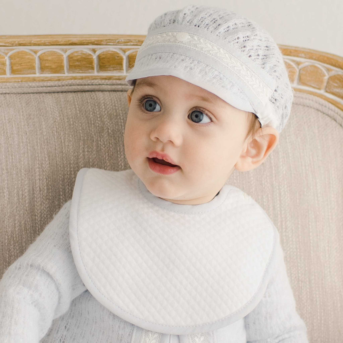 Close-up of a baby wearing the Harrison Bib, showcasing the quilted white fabric with soft gray edging. The bib sits neatly over a delicate outfit, adding a classic touch to the ensemble.