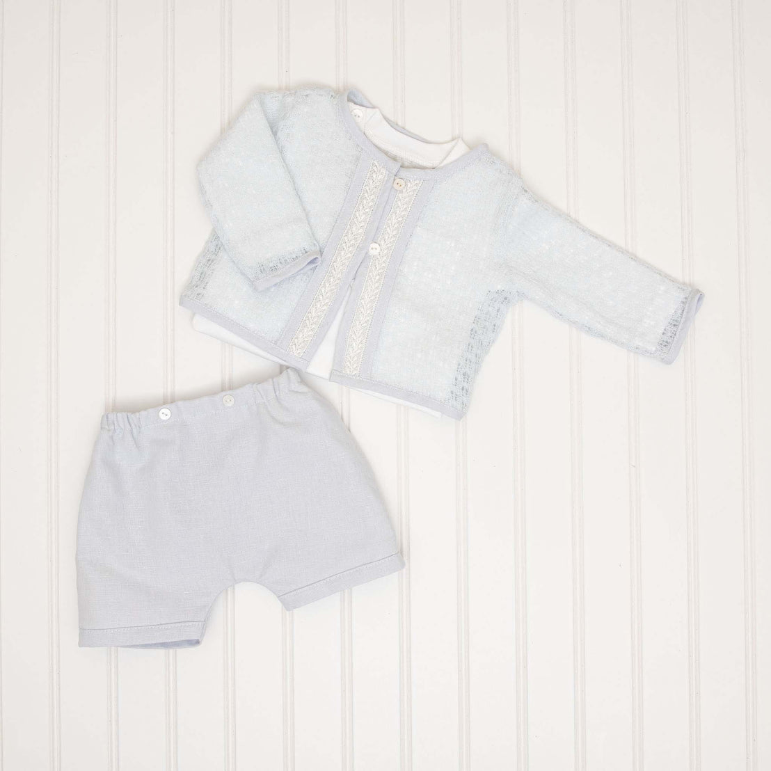 A flat lay of the Harrison Sweater 3-Piece Shorts Suit, featuring the light blue knit sweater with lace trim, coordinating shorts, and a matching onesie.