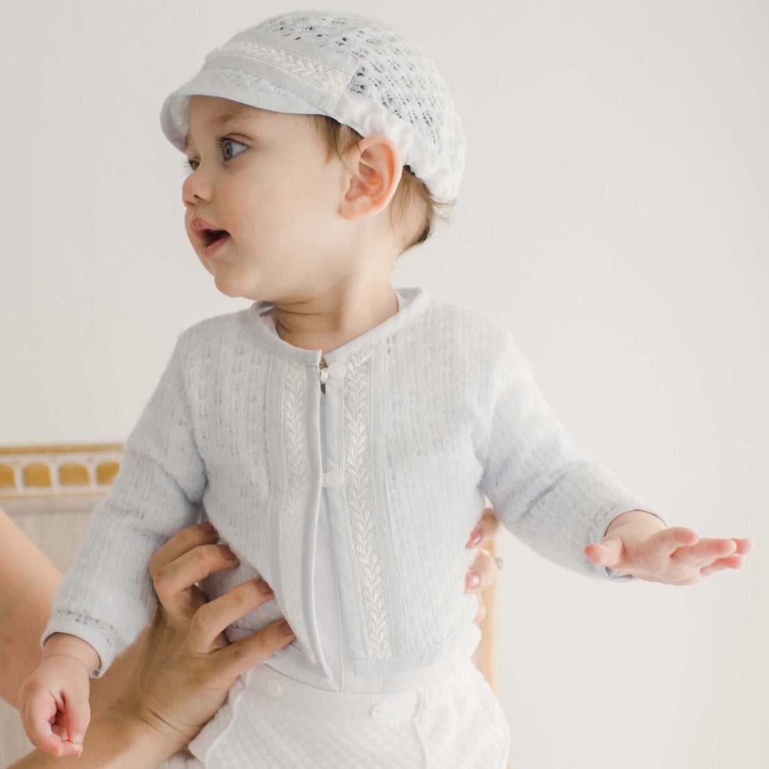 A baby being held while wearing the Harrison Sweater 3-Piece Pant Suit, showing the front details of the blue knit sweater and quilted pants.