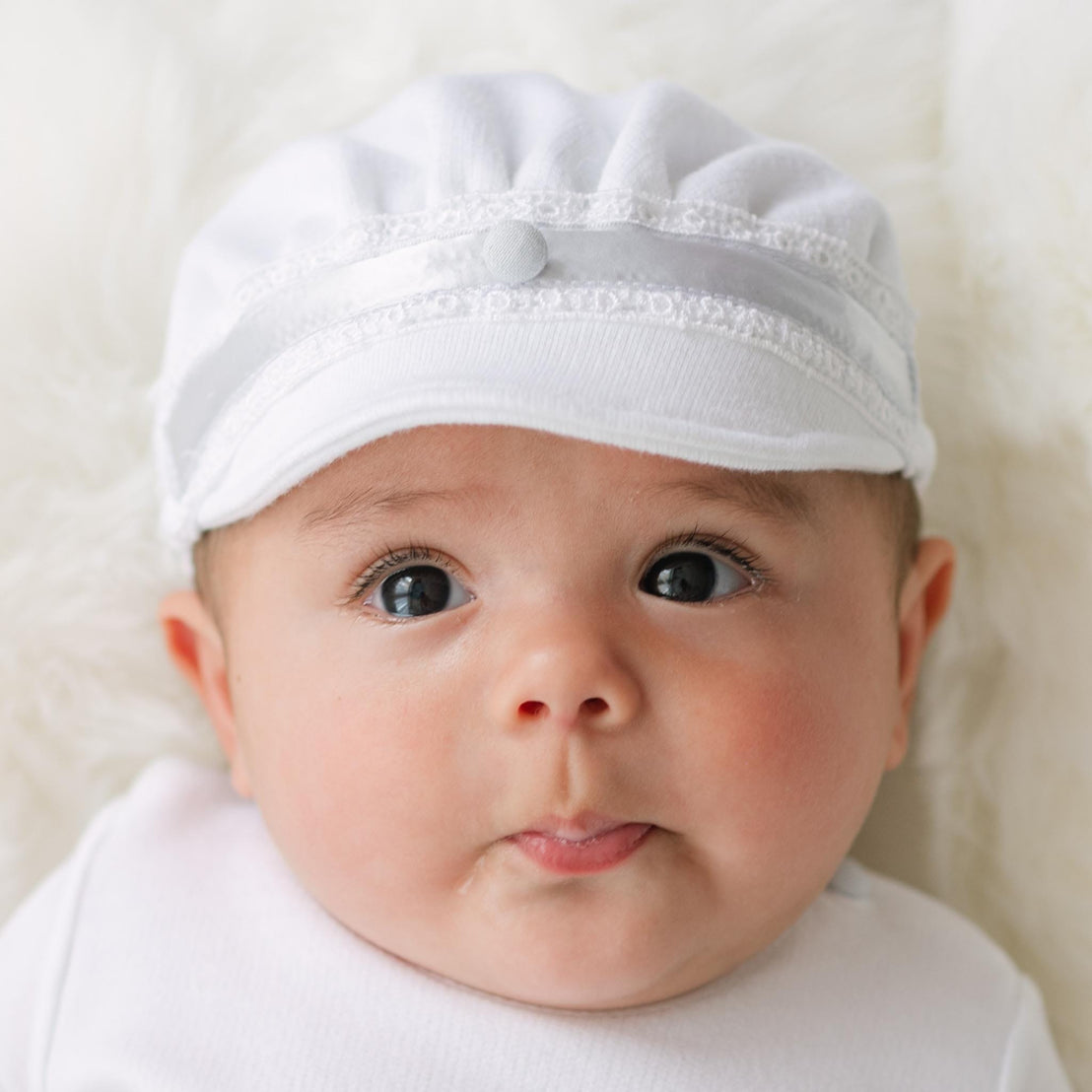 Baby wearing the Henry Brim Cap with lace details on a plain background.