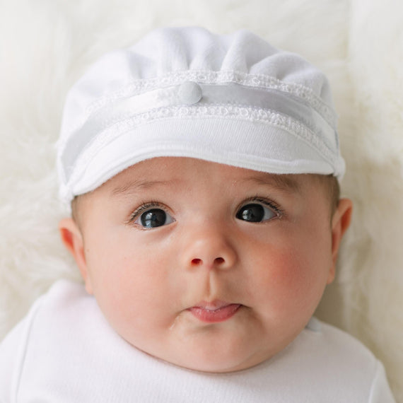 Baby wearing the Henry Brim Cap with lace details on a plain background.