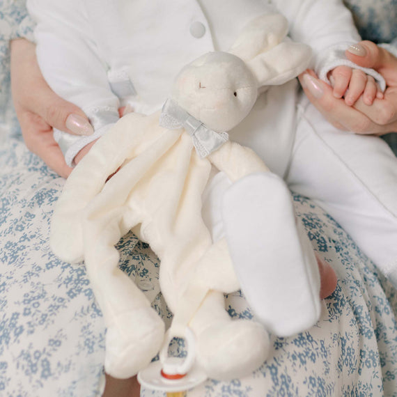 Close up photo of the Henry Silly Bunny Buddy held by a baby sitting on his mother's lap. Details show the lace and blue silk ribbon bow tie. Perfect as unique baby gifts.