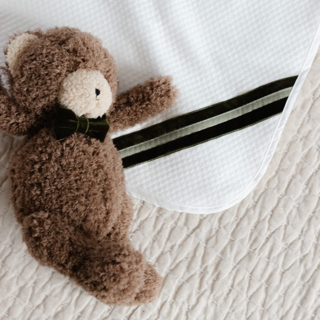 Brown teddy bear with a bow tie on a white quilt blanket
