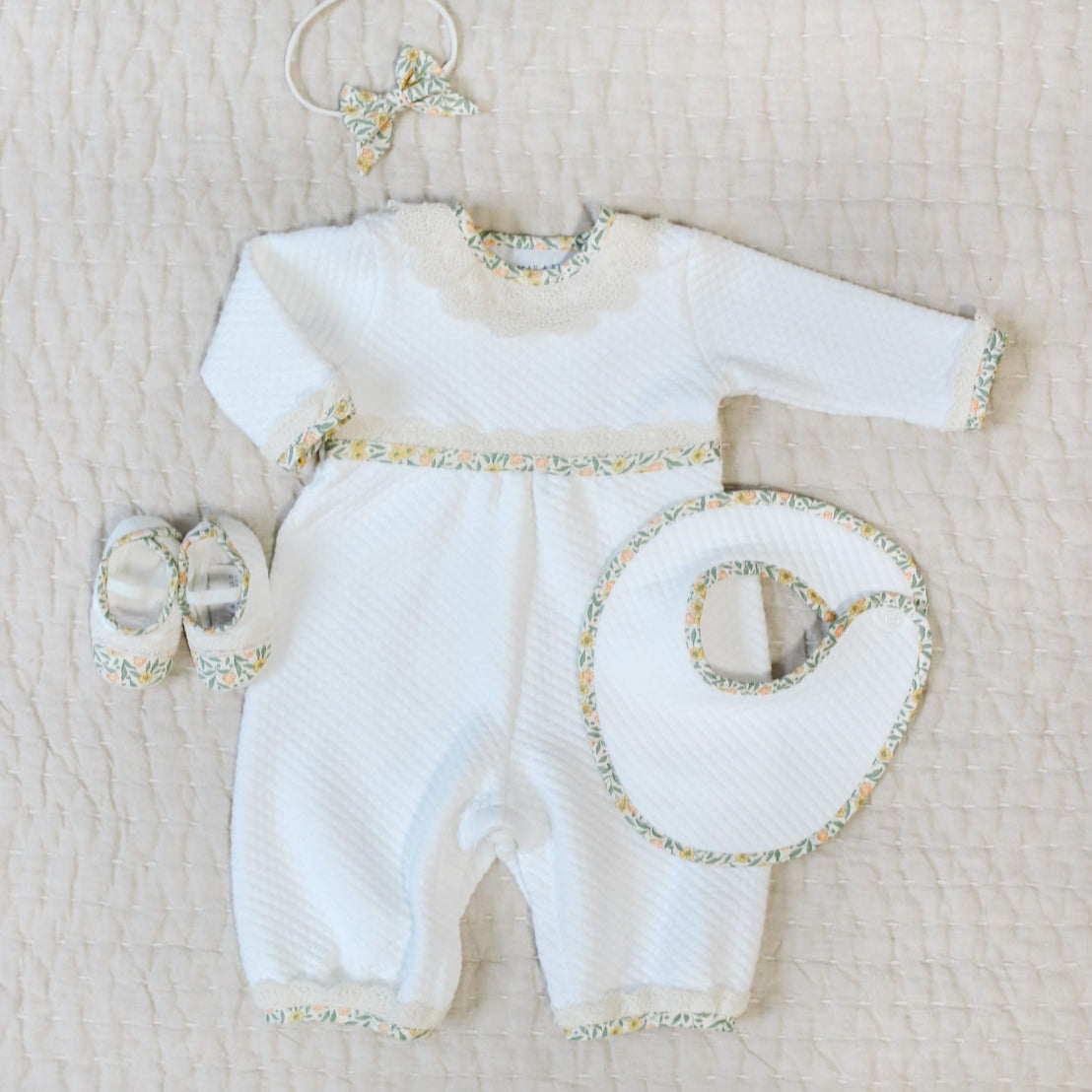 Flat lay photo of the Lillian Romper and matching Bib, Booties, and Headband. Details show yellow floral cotton trim.  