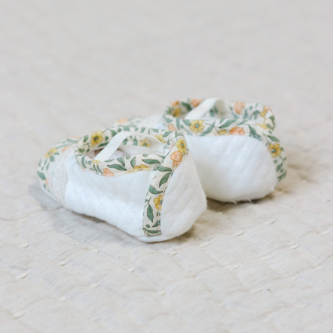 Flat lay photo showing the back of the Lillian Booties with yellow floral cotton trim. Set against a beige linen background.