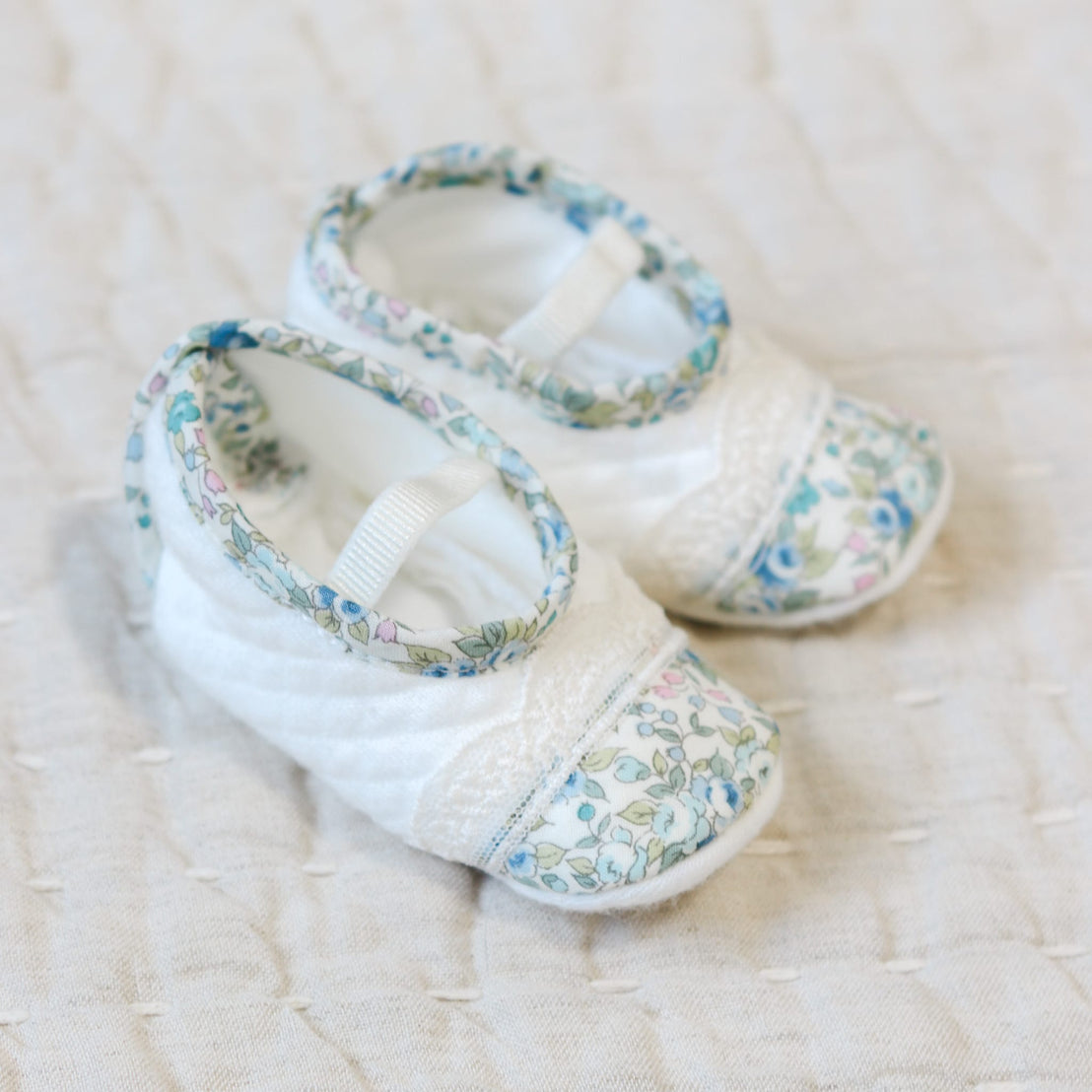Flat lay photo of the Lillian Booties with blue floral cotton trim. Set against a beige linen background.