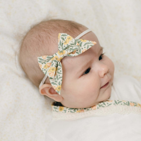 Baby wearing the yellow Lillian Bow Headband and matching Layette on a light background. Details show 