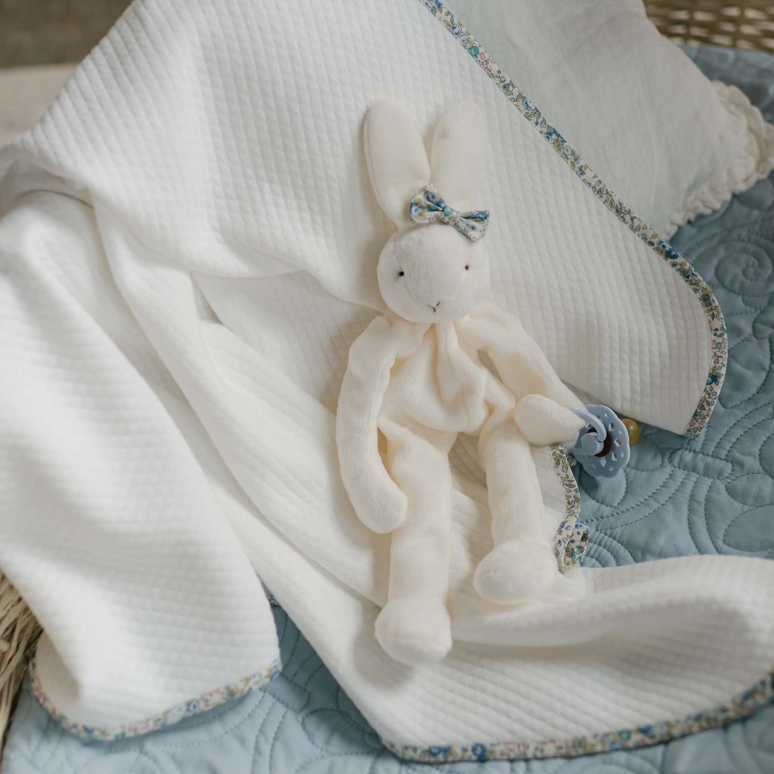 The Petite Fleur Blue Personalized Blanket with floral trim, shown draped with a plush bunny holding a pacifier.