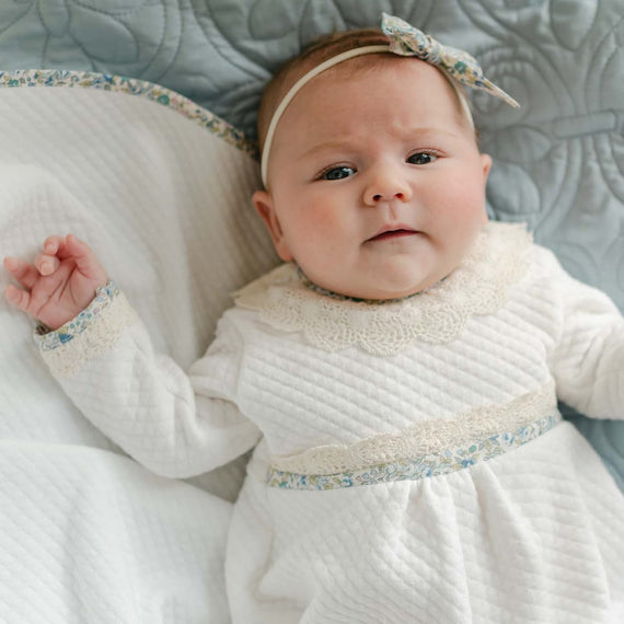Baby lying in a basket wearing the Petite Fleur Blue Romper with matching shoes and floral bow headband.