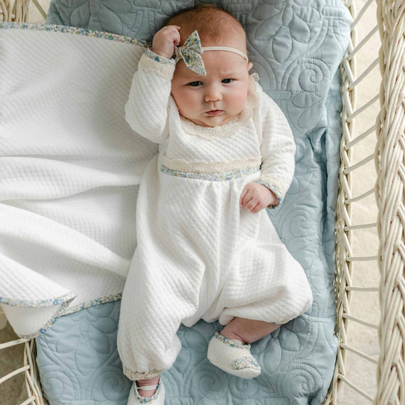 Baby lying in a basket wearing the Petite Fleur Blue Romper with matching shoes and floral bow headband.