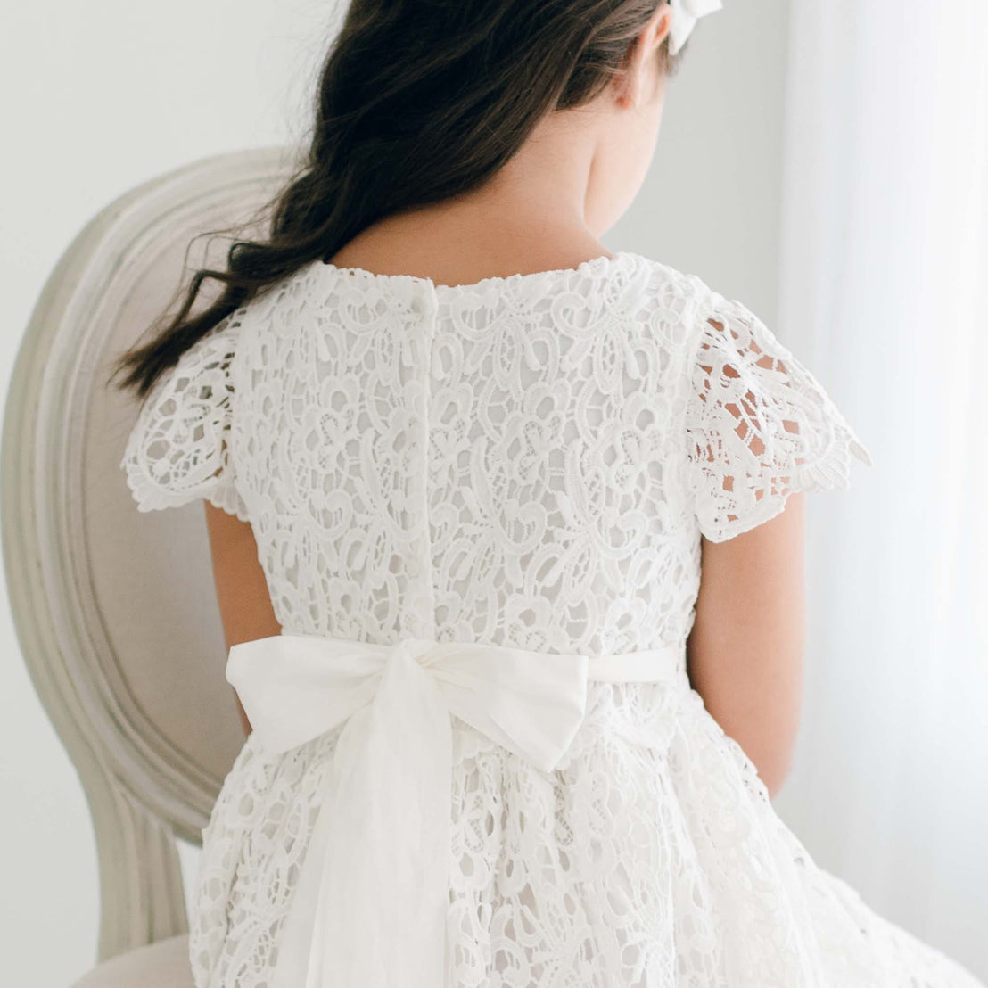 Close-up of the back of the Lola Girls Lace Dress, showing the lace detail and white sash bow.