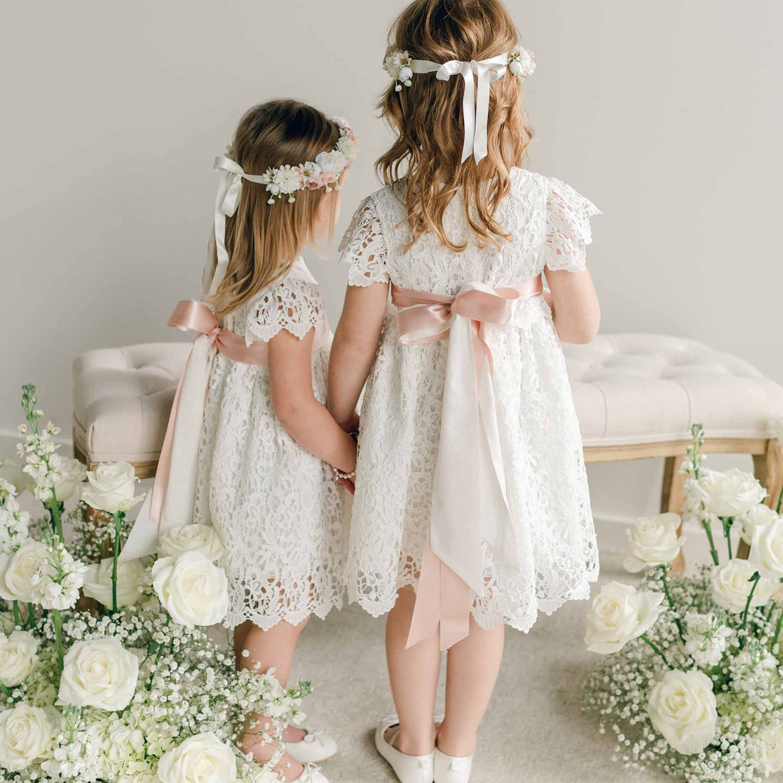 Back view of two young girls holding hands in the Lola Girls Lace Dress, showing long satin bow details.