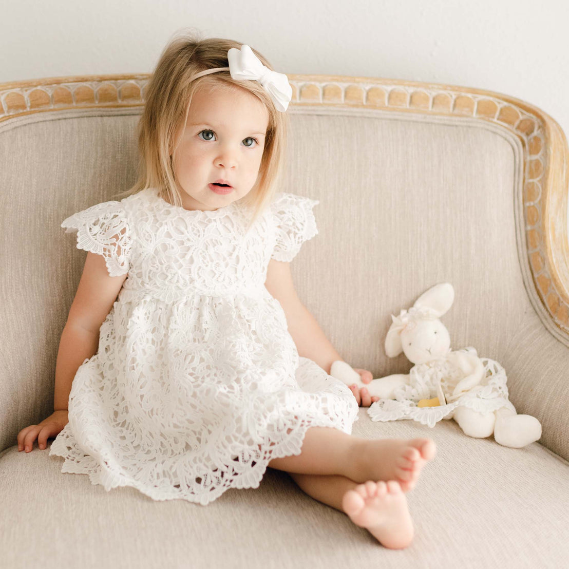 Baby girl wearing the Lola Dress. She is holding a Lola Silly Bunny Buddy pacifier holder with the same Lola Dress.