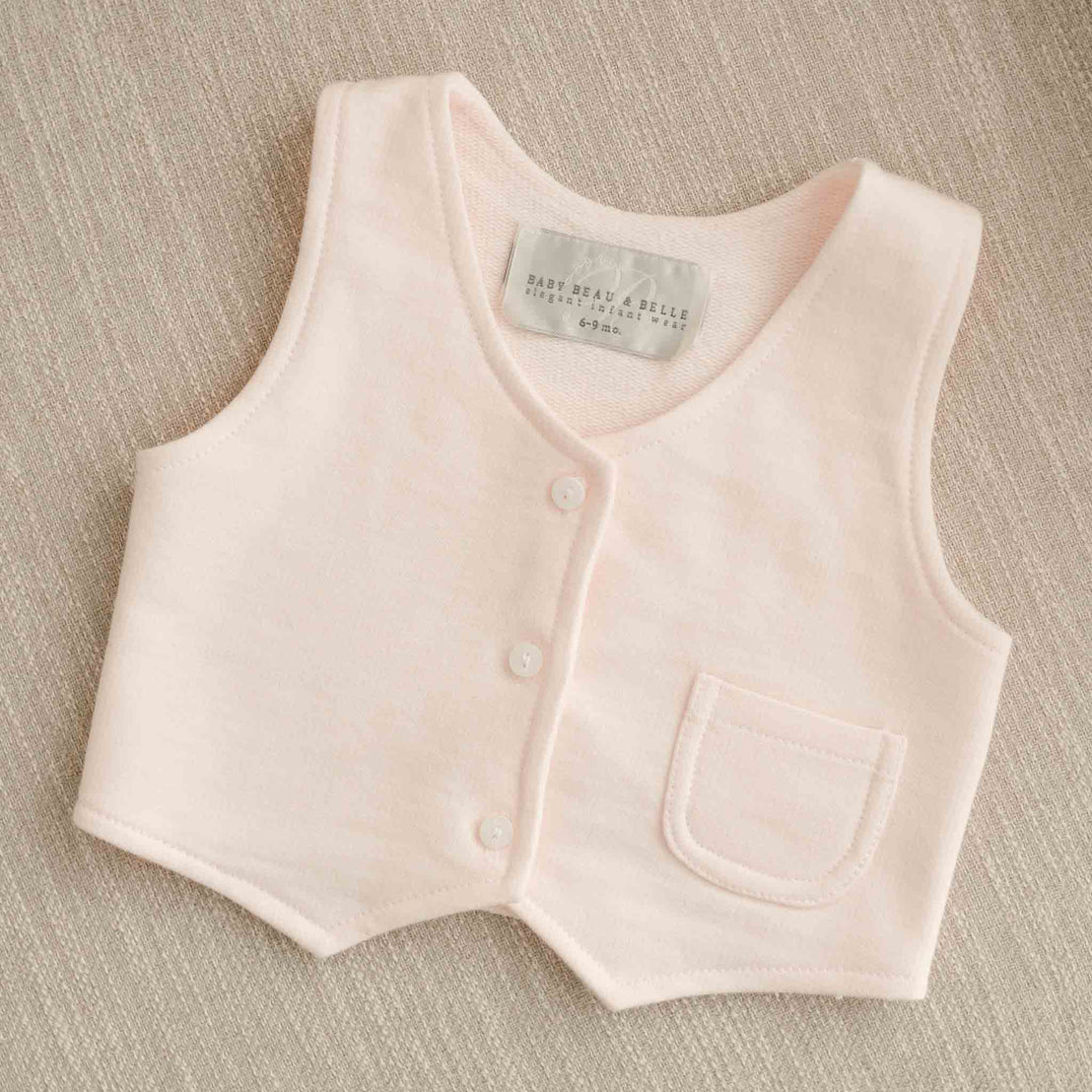 The Milo Blush Vest displayed on a neutral fabric background, highlighting its soft texture and button details.